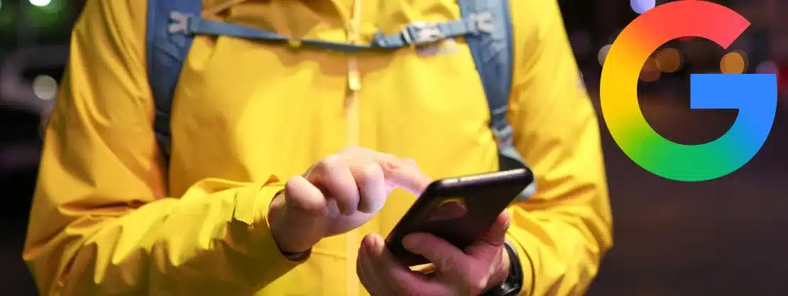 Person in yellow jacket using smartphone with Google logo in the top right corner.